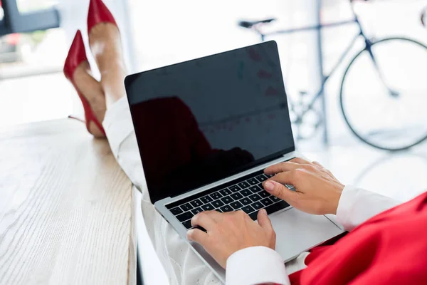 Обрезанный образ бизнесвумен с помощью ноутбука и сидя с ногами на столе в офисе — стоковое фото