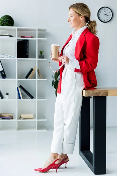 Вид сбоку красивой бизнесвумен, стоящей с кофе в бумажной чашке в офисе — стоковое фото