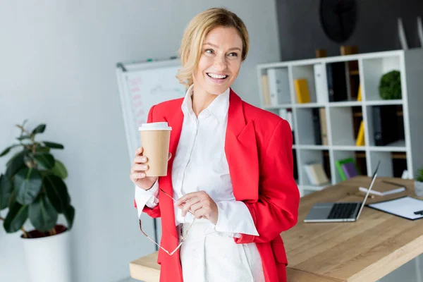 Atractiva mujer de negocios de pie con café en taza de papel en la oficina - foto de stock