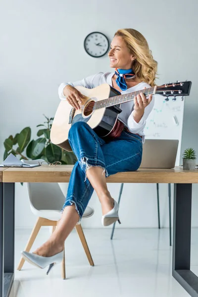 Lächelnde attraktive Geschäftsfrau spielt Akustikgitarre im Büro — Stockfoto