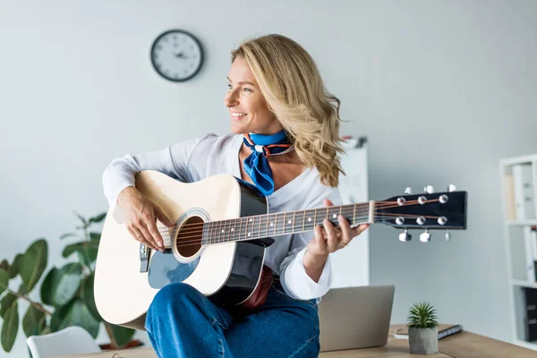 Happy attractive businesswoman playing acoustic guitar in office — Stock Photo