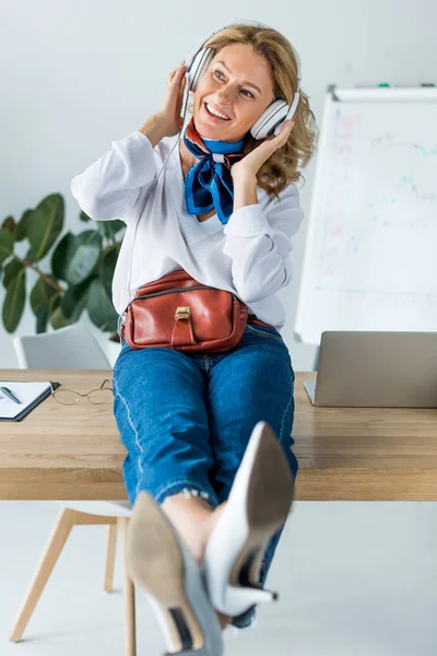 Красивая счастливая деловая женщина слушает музыку в наушниках в офисе — стоковое фото