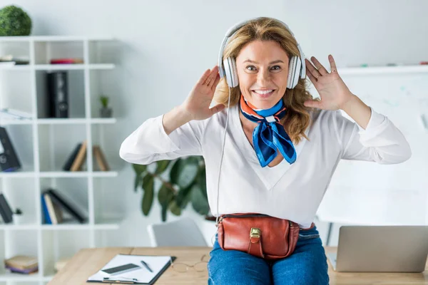 Attrayant femme d'affaires heureuse écouter de la musique dans les écouteurs au bureau — Photo de stock