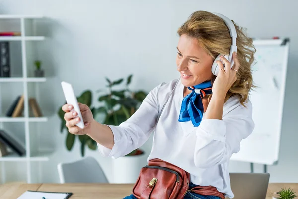 Schöne Geschäftsfrau mit Kopfhörer macht Selfie mit Smartphone im Büro — Stockfoto