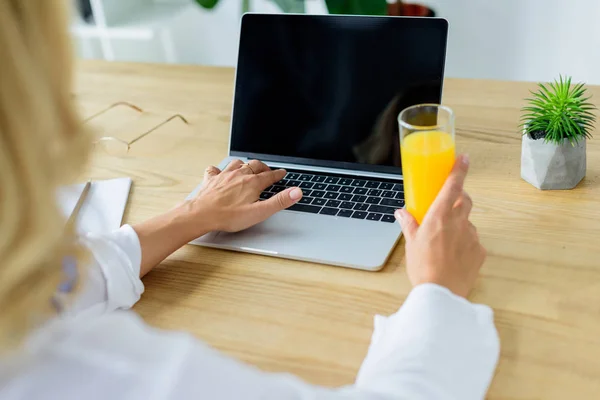 Imagem cortada de empresária trabalhando com laptop e segurando vidro de suco no escritório — Fotografia de Stock