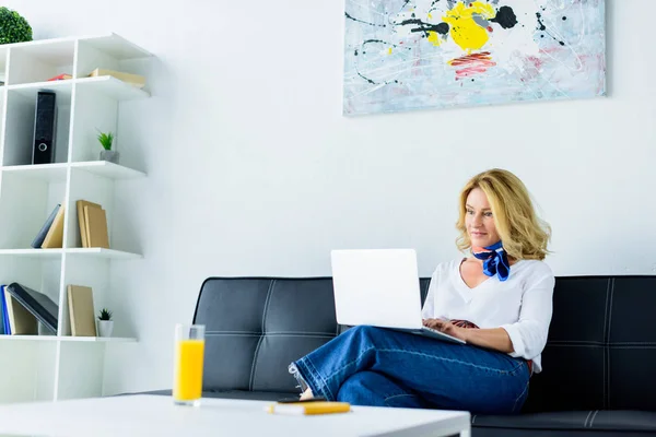 Attractive businesswoman sitting on sofa in office and working with laptop — Stock Photo