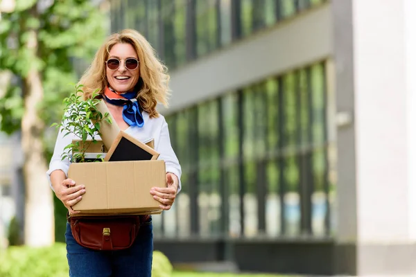 Donna attraente sorridente che tiene la scatola di carta con roba da ufficio sulla strada — Foto stock