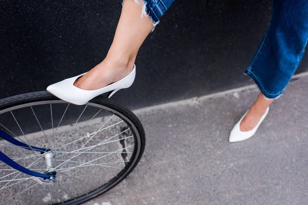 Cropped image of woman in white shoes touching bicycle wheel on street — Stock Photo