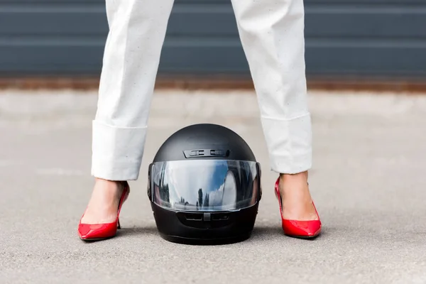 Cropped image of woman in red shoes standing near motorcycle helmet on street — Stock Photo