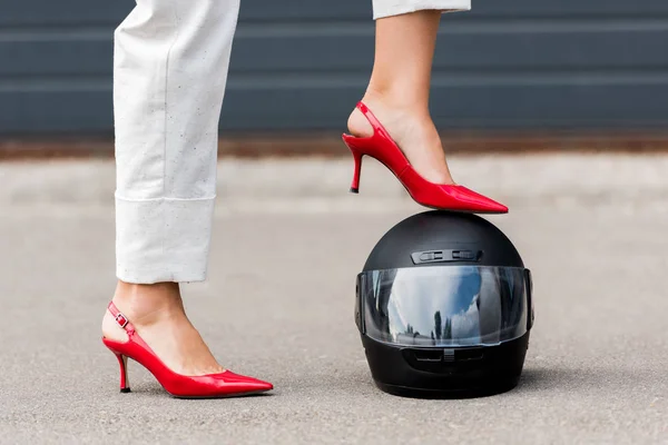 Cropped image of woman in red high heels putting leg on motorcycle helmet on street — Stock Photo