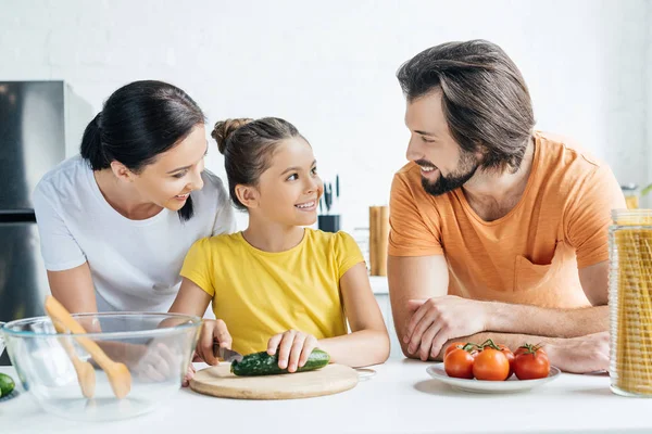 Happy young family cooking healthy dinner together at kitchen and looking at each other — Stock Photo