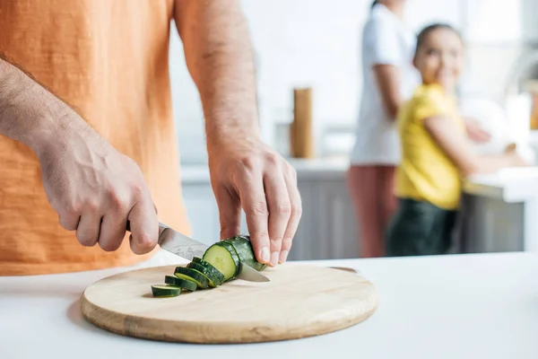 Tiro cortado de pai cortando pepino para salada, enquanto sua esposa e filha lavar pratos na cozinha — Fotografia de Stock