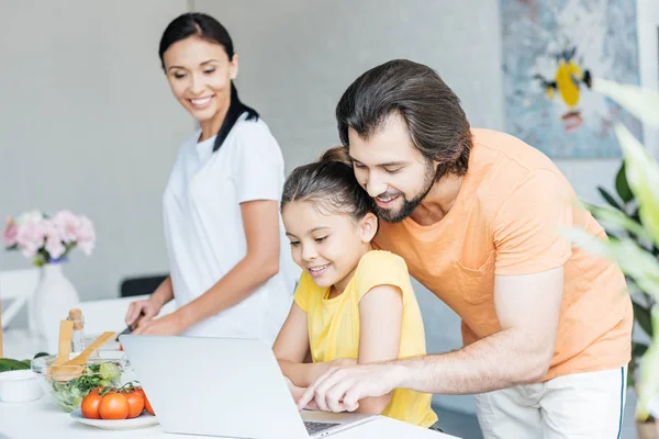 Familia joven feliz usando el ordenador portátil juntos en la cocina - foto de stock