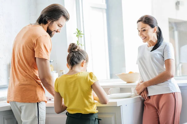 Attractive young family washing dishes together at kitchen — Stock Photo