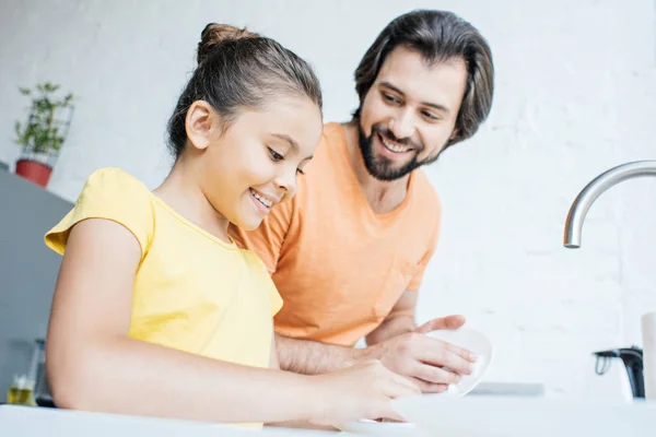 Padre e hija lavando platos juntos en casa - foto de stock