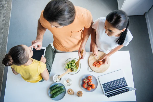 Visão de alto ângulo de bela família jovem com gadgets cozinhar juntos na cozinha — Fotografia de Stock