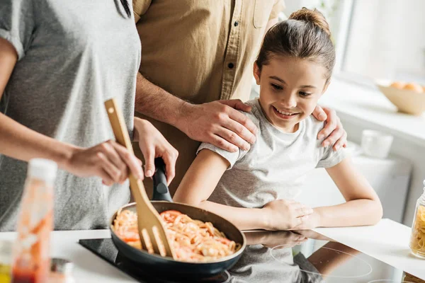 Обрезанный снимок семьи с маленькой дочерью, готовящей омлет на кухне — стоковое фото