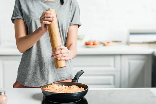 Colpo ritagliato di donna che aggiunge pepe alla cottura della pasta sulla padella — Foto stock