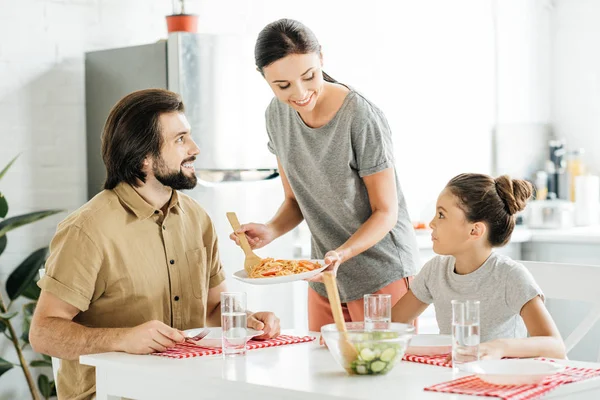 Attrayant jeune mère avec délicieux petit déjeuner pour la fille et le mari à la cuisine — Photo de stock