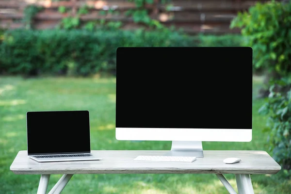 Enfoque selectivo de la computadora portátil y la computadora con pantallas en blanco en la mesa al aire libre - foto de stock