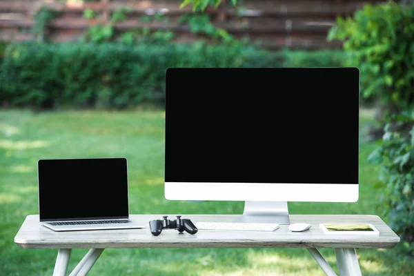 Enfoque selectivo de joystick, tableta digital, ordenador y portátil con pantallas en blanco en la mesa al aire libre - foto de stock