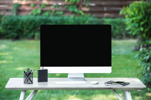 Enfoque selectivo de frasco, libro de texto, smartphone y computadora con pantalla en blanco en la mesa al aire libre - foto de stock