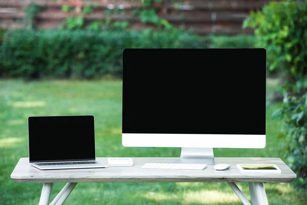 Enfoque selectivo de la computadora portátil y la computadora con pantallas en blanco en la mesa al aire libre - foto de stock