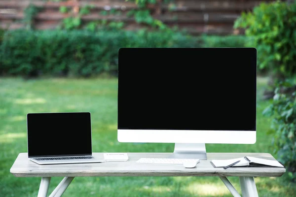 Selective focus of textbook, laptop and computer with blank screens at table outdoors — Stock Photo