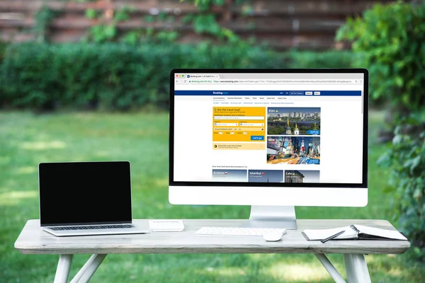 Enfoque selectivo de la computadora portátil con computadora de pantalla en blanco con booking.com sitio web en la mesa al aire libre - foto de stock