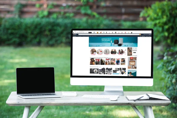 Enfoque selectivo de la computadora portátil con computadora de pantalla en blanco con sitio web amazon en la mesa al aire libre - foto de stock