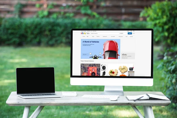 Foco selectivo del ordenador portátil con la computadora de la pantalla en blanco con el Web site de eBay en la tabla al aire libre - foto de stock