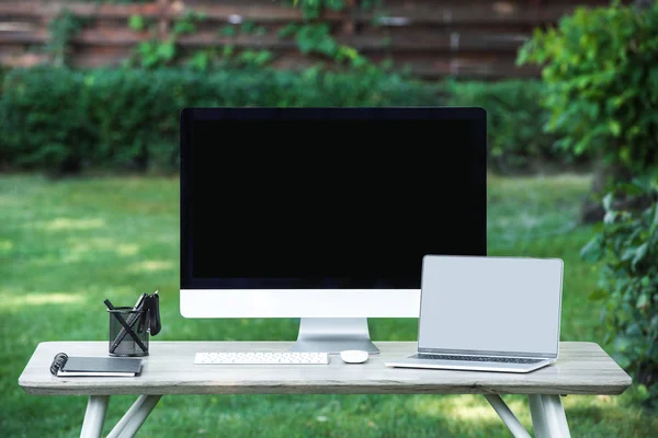 Selective focus of textbook, laptop and computer with blank screens at table outdoors — Stock Photo