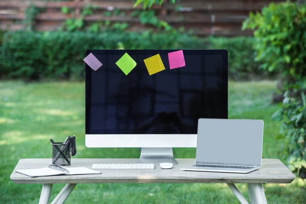 Selective focus of textbook, laptop and computer with blank screens and stick it notes at table outdoors — Stock Photo