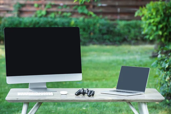 Selective focus of joystick, computer and laptop with blank screens on table outdoors — Stock Photo