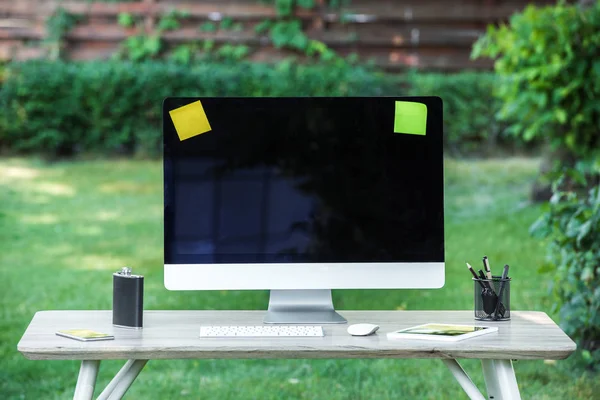 Selective focus of flask, digital tablet, computer with blank screen, stick it notes and smartphone on table outdoors — Stock Photo