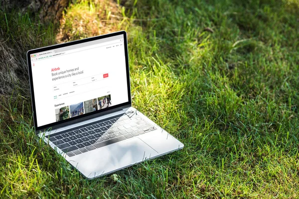 Vue rapprochée de l'ordinateur portable avec airbnb site Web sur l'herbe à l'extérieur — Photo de stock