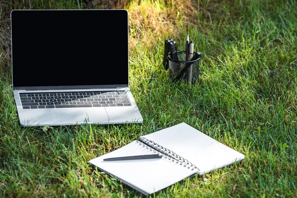 Close up view of laptop with blank screen and empty textbook with pen on grass outdoors — Stock Photo