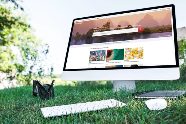 Selective focus of textbook and computer with shutterstock website on grass outdoors — Stock Photo