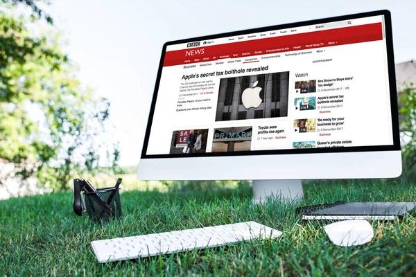 Selective focus of textbook and computer with bbc news website on grass outdoors — Stock Photo