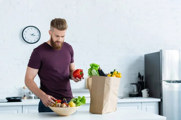 Bonito jovem barbudo homem segurando legumes frescos na cozinha — Fotografia de Stock