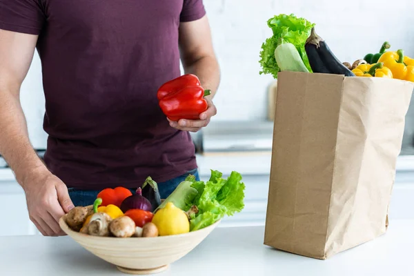 Colpo ritagliato di giovane uomo mettendo verdure fresche dalla borsa della spesa in ciotola — Foto stock