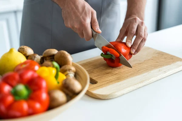 Cropped shot of man cutting bell pepper on wooden cutting board — Stock Photo
