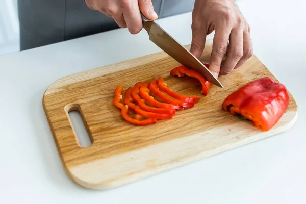 Primer plano vista parcial de hombre corte pimiento sobre tabla de cortar de madera - foto de stock