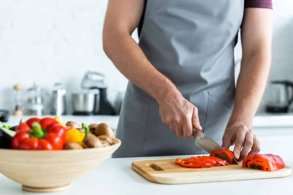 Cropped shot of man in apron cutting vegetables in kitchen — Stock Photo