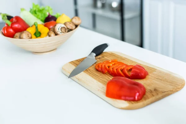 Vista de cerca de pimiento y cuchillo en rodajas sobre tabla de cortar de madera - foto de stock