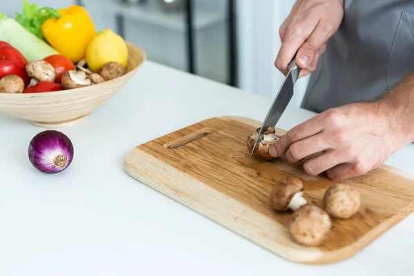 Close-up partial view of man cutting fresh mushrooms on wooden cutting board — Stock Photo