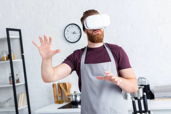 Young man in apron using virtual reality headset in kitchen — Stock Photo