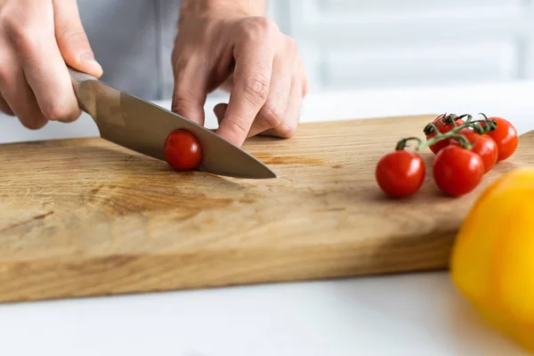 Gros plan vue partielle de l'homme découpant la tomate cerise sur une planche de bois — Photo de stock