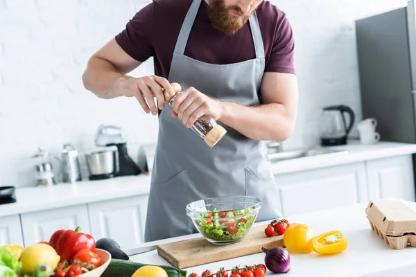 Tiro recortado de barbudo hombre en delantal de cocina ensalada de verduras - foto de stock