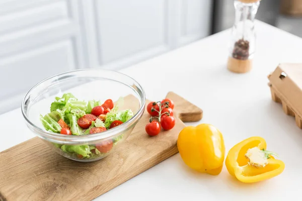 High angle view of glass bowl and fresh vegetables on wooden cutting board — Stock Photo